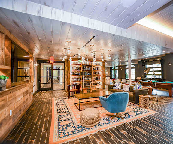 The Crosby at The Brickyard entertainment and seating space The resident lounge with a gray couch fun overhead lighting, bookshelves, a pool table, a coffee table, an electric blue chair, lamps, a pool table, and windows at the Crosby at the Brickyard Apartment Homes.