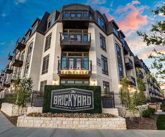 The Crosby at The Brickyard A cinematic shot of the front of the Crosby at the Brickyard Apartment Homes with a black sign and plants surrounding.