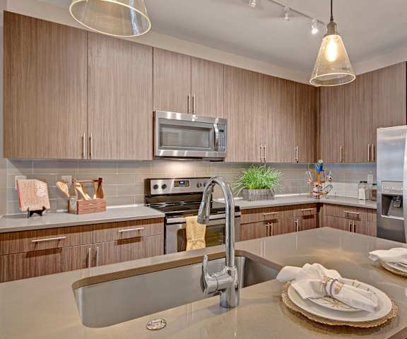 A large kitchen with stainless steel appliances, marble countertops, large wooden cabinets, decorations, a plant, and two place settings at River House Apartment Homes. 