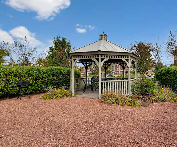 The white gazebo surrounded by bushes with a grill off to the left at Swan Creek Apartment Homes. 