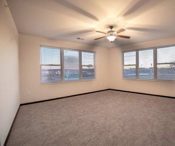 A large, empty carpeted bedroom with overhead lighting, with a ceiling fan, and two windows at the Park Apartment Homes. 