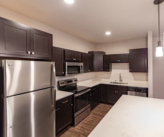 A large, modern kitchen with stainless steel appliances, kitchen utensils, white countertops with lots of room, a kitchen island, and large, dark wooden cabinets at the Park Apartment Homes. 
