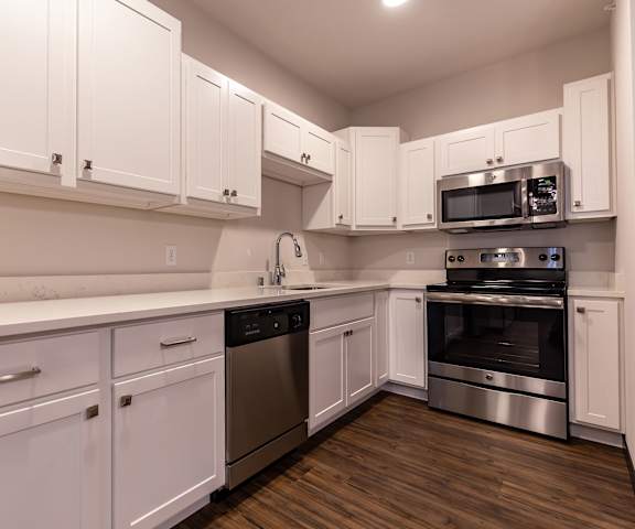 A large, modern kitchen with stainless steel appliances, kitchen utensils, white countertops with lots of room, a kitchen island, and large, white wooden cabinets at the Park Apartment Homes. 