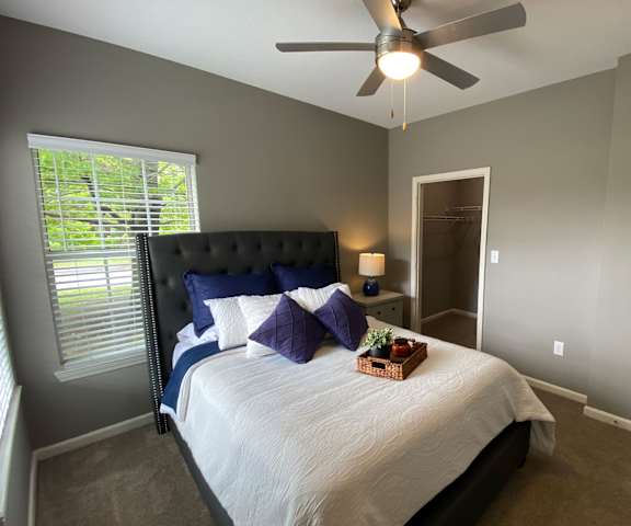 A bedroom with a queen-size bed, a dresser, decorations, closet, window, and nightstands at Harbin Pointe Apartment Homes. 