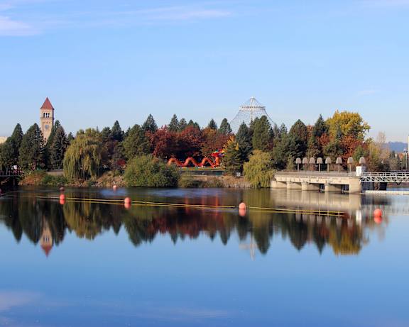 A serene lake with a bridge and a church tower in the background.