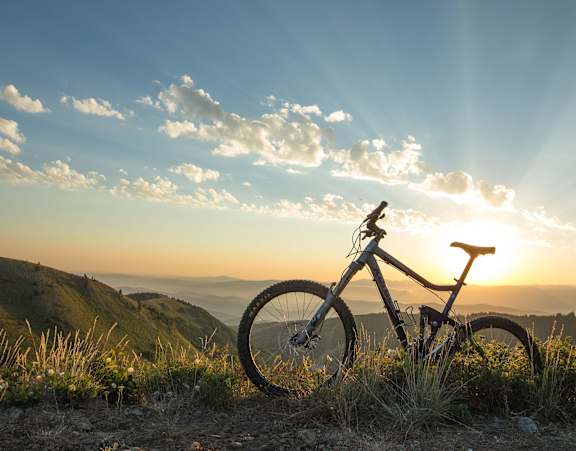 A bicycle is parked on a grassy hill with the sun shining through the clouds.