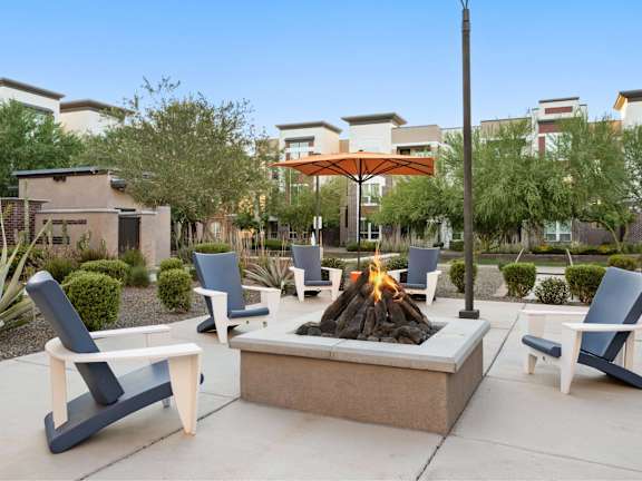 A patio with a fire pit and chairs.