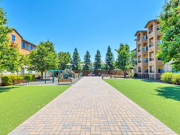 an empty park with trees and a playground in front of an apartment building