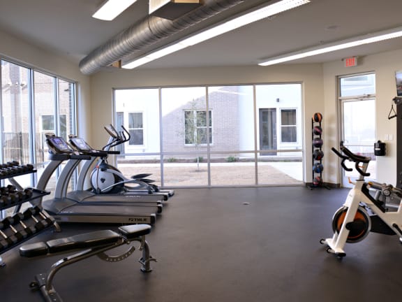 a gym with cardio equipment and a window view of a building at Epic Apartments, Texas, 76210
