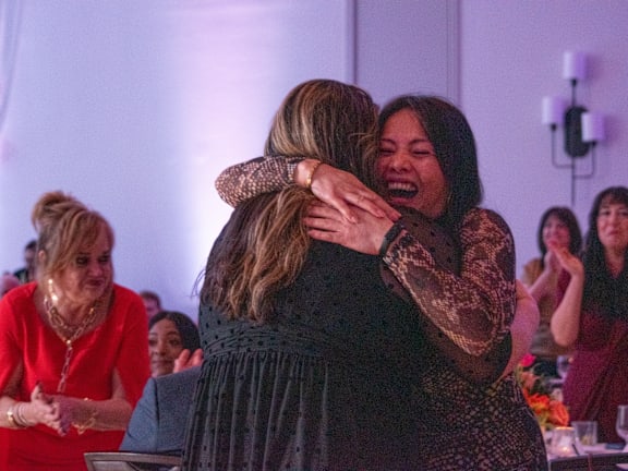 Two women hug each other in a room with purple lighting.