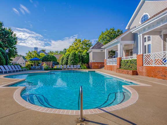 A large outdoor swimming pool surrounded by a brick wall and lounge chairs.