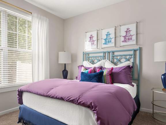 A bed with a purple comforter and a white pillow.