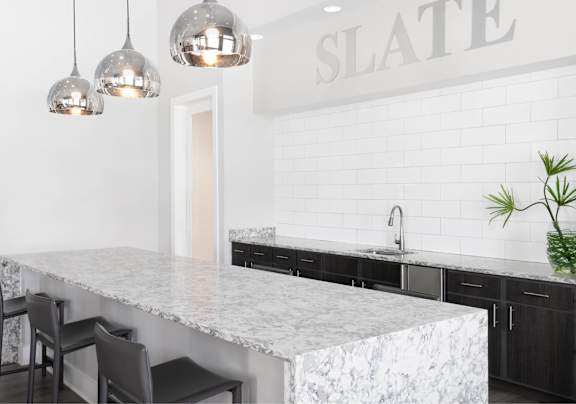 A kitchen with a marble countertop and pendant lights.