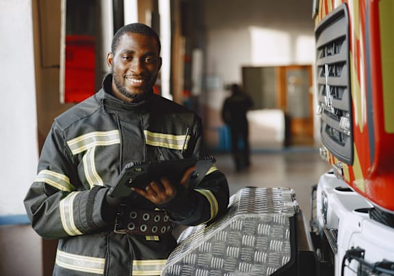 A man in a firefighter's uniform is standing in a garage with a fire truck.