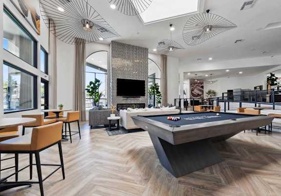 A pool table is in the middle of a room with a bar and a television.