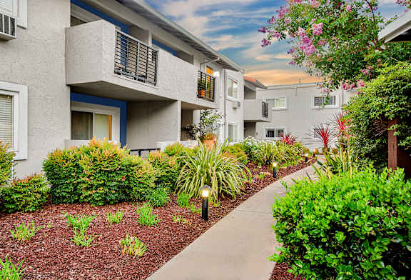 A concrete pathway leads through a landscaped area in front of apartment buildings.