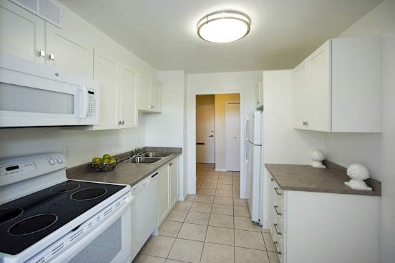a kitchen with white cabinets and white appliances and a long hallway