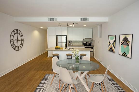 a dining room with a glass table and chairs and a kitchen in the background