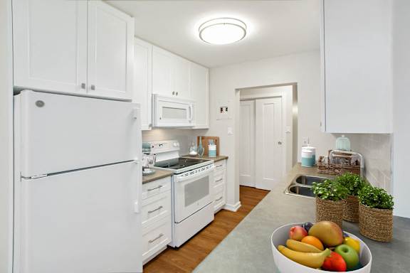 A kitchen with white appliances and a bowl of fruit on the counter.