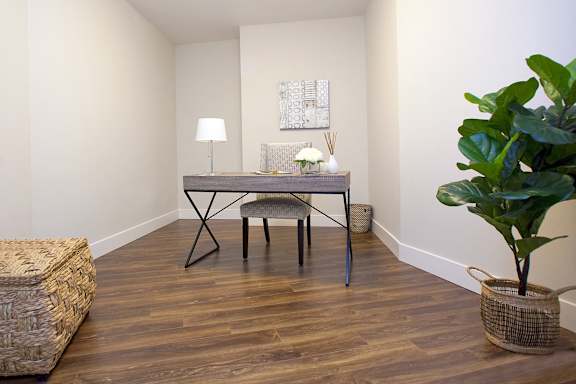 A room with a wooden floor and a table with a lamp and a plant on it.