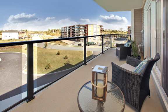 A balcony with a chair and table overlooking a parking lot and buildings.