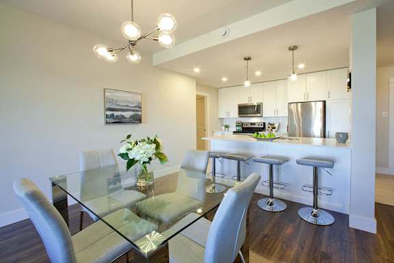 A modern kitchen with a glass dining table and grey chairs.