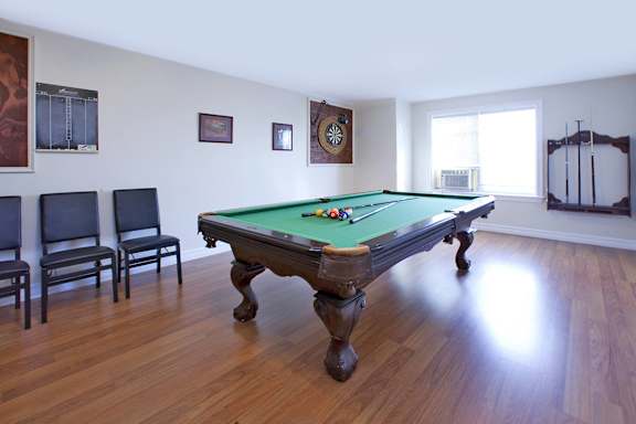 A pool table in a room with chairs and a clock on the wall.