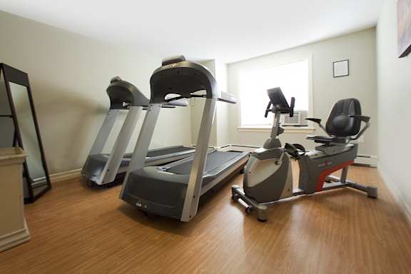A room with a treadmill, a stationary bike and a chair.