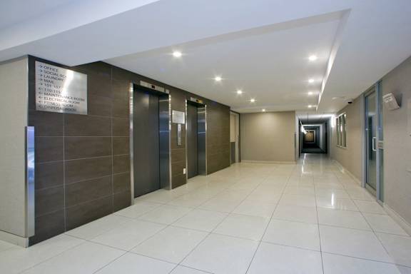 a long corridor with elevators and a white tiled floor in a building