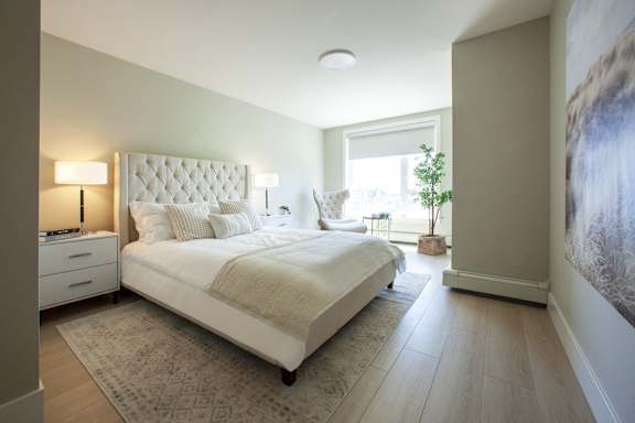 A large bed with a white headboard and pillows in a bedroom with a rug on the floor.