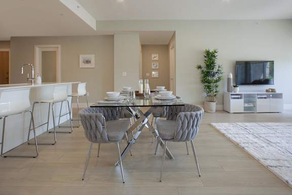 A modern dining room with a glass table and grey chairs.