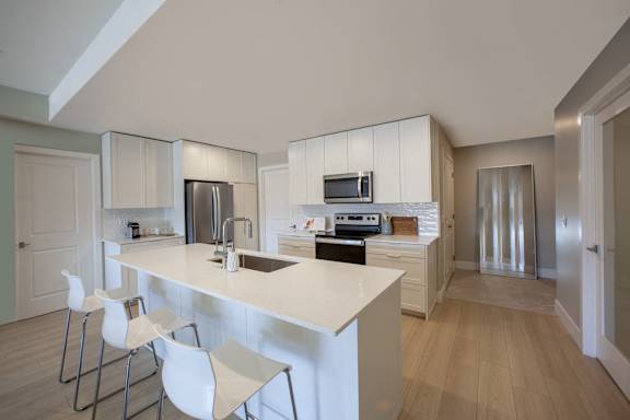 A modern kitchen with a white countertop and white chairs.