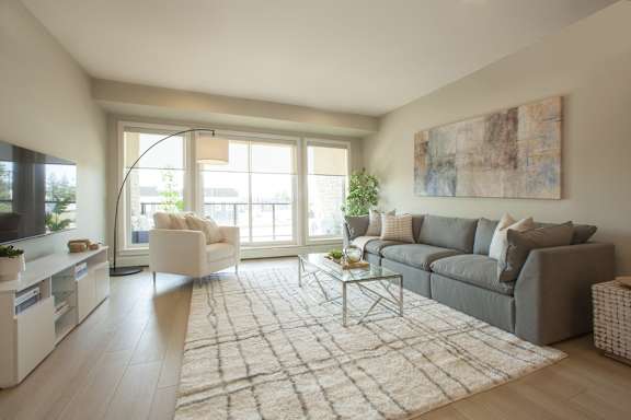 A living room with a grey couch, a white chair, and a large window.