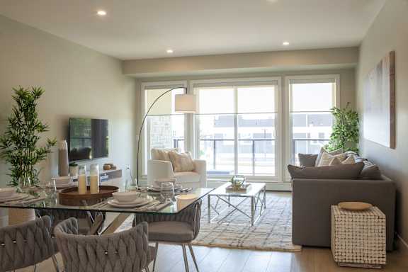 A modern living room with a glass dining table and grey chairs.