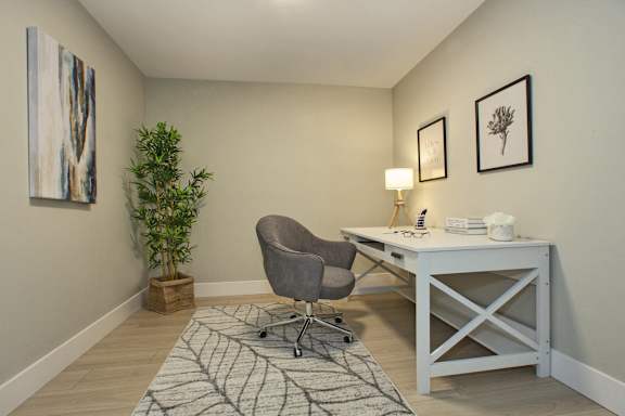 A grey chair is in front of a desk with a lamp and a plant on it.