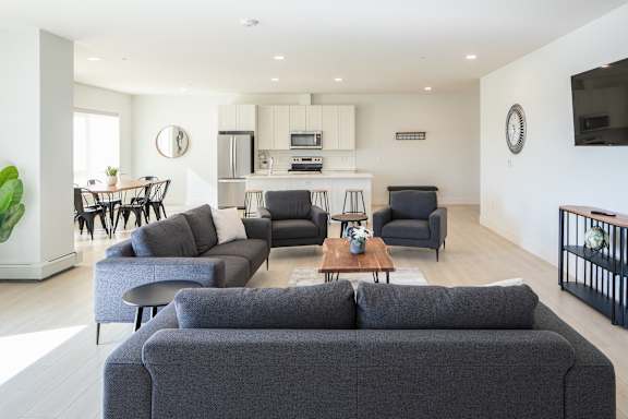 A modern living room with a grey sofa and a kitchen in the background.