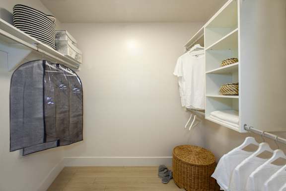 A white closet with clothes and a basket on the floor.