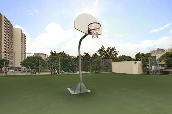 A basketball hoop stands on a green court with a tall building in the background.
