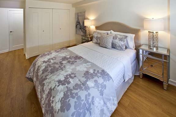 A bed with a grey and white comforter is in the middle of a room with a wooden floor.