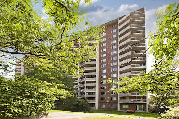 A tall apartment building is surrounded by trees and greenery.
