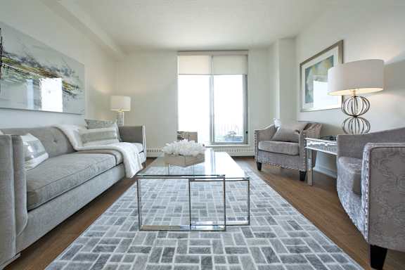 A living room with a grey sofa, a glass coffee table, and a grey rug.