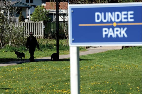 a person sitting in the grass near a dundee park sign