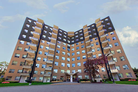 A large, modern apartment building with a symmetrical design and a landscaped courtyard in front.