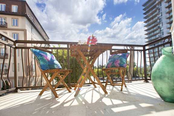 A wooden table and two chairs with colorful cushions are on a balcony.