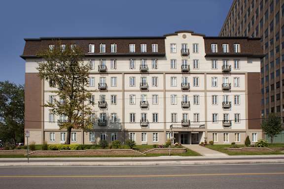 A large, multi-story building with a brown and beige exterior and a tree in front of it.