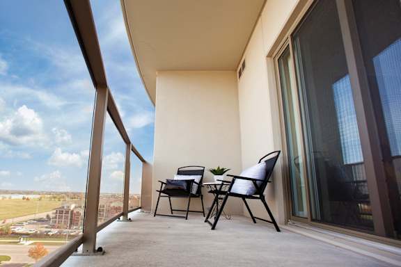 A balcony with a table and chairs overlooking a field.