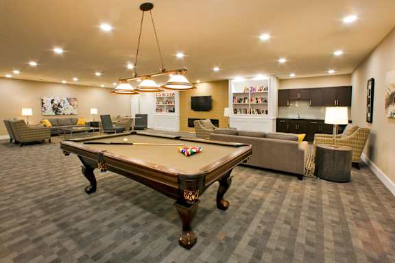 A pool table is in the middle of a room with a television and a bookshelf.