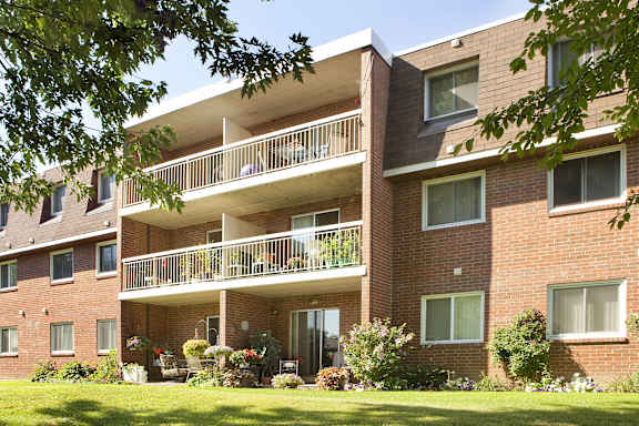 A red brick building with a balcony and a garden in front.