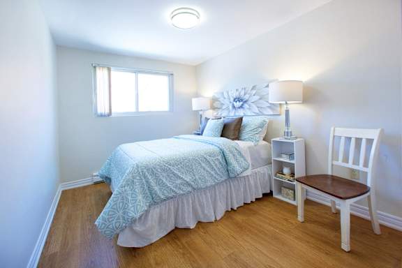 A bedroom with a bed, nightstand, chair, and window.