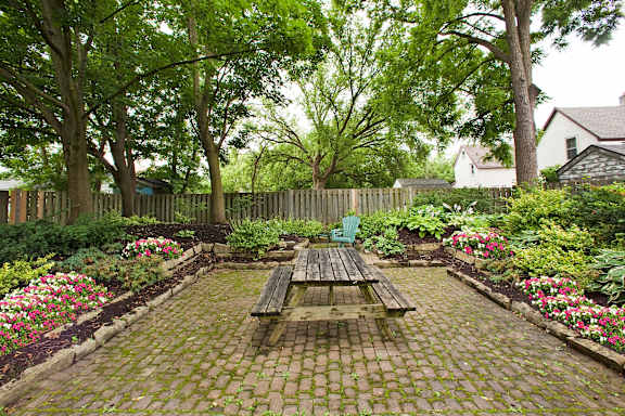 A wooden picnic table sits in the middle of a brick patio.